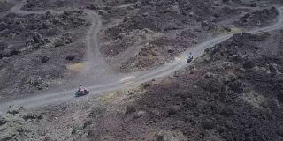 一对夫妇骑着摩托车在通往金塔马尼火山的黑色熔岩路上行驶