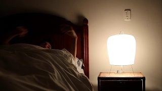年轻人躺在床上，关掉床头柜里的灯。一个人躺着睡觉的时候在想一些事情视频素材模板下载