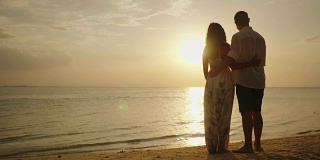一对年轻的夫妇站在海滩上，欣赏海面上的日落