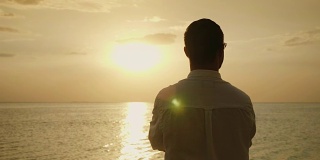 斯坦尼康镜头:孤独的男人期待着海面上的日落。后视图。浪漫和海上度假。4K慢动作视频