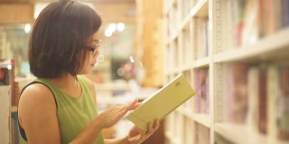 亚洲妇女在书店看书对书架的背景。