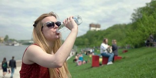 夏日里，戴着太阳镜的年轻女子从塑料瓶里喝水