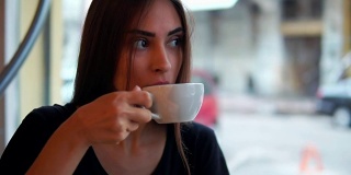 近距离观看有吸引力的年轻女子梦想与一杯热咖啡坐在窗前的咖啡店。在漫长忙碌的一天之后休息一下。喝杯热茶放松一下
