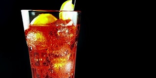 在慢镜头中，饮用一杯spritz aperitif aperol橙鸡尾酒与冰块，与泡沫运动的黑色背景，假期和夏季时间