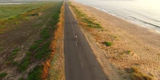 4K无人机拍摄的女人在阳光大道上骑车