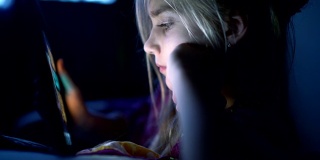 十几岁的女孩晚上在床上用平板电脑看书