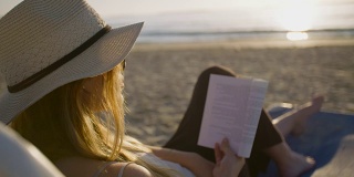 年轻迷人的女人坐在美丽的海滩上看书