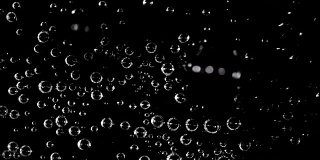 俯视图，苏打水在玻璃杯里。把水倒到泡泡上产生的气泡会漂浮起来，形成黑色背景的波浪。4 k 30 fps决议。