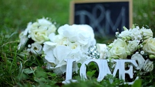 婚礼装饰字爱，鲜花和木质牌匾与字母D和M在公园的绿草背景视频素材模板下载