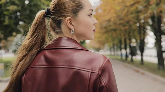 秋天来了。穿着酒红色夹克的漂亮女人走在城市街道上，慢镜头，后视镜