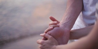 男性和女性的手的特写视图。年轻的夫妇站在海边，在海滩上，手牵着手
