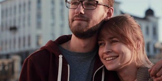 这是一对年轻美丽的夫妇站在市中心向一边看的肖像。日落时分，快乐的男人和女人拥抱在一起