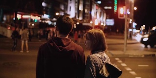 年轻时尚的夫妇站在等待红绿灯的背影。美丽的男女在傍晚过马路