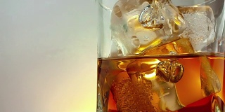 特写的酒保倒威士忌在饮用玻璃与冰块在温暖的白色背景，时间放松喝威士忌