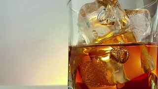 特写的酒保倒威士忌在饮用玻璃与冰块在温暖的白色背景，时间放松喝威士忌视频素材模板下载