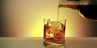 酒吧间招待员将威士忌酒瓶倒入玻璃杯中，冰块放在温暖的金色背景上，放松的时间喝威士忌
