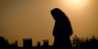 年轻苗条的女子在傍晚散步，背景是城市风景，映衬着太阳的轮廓