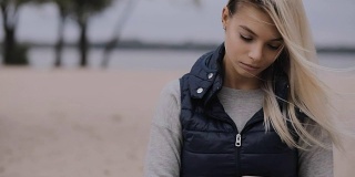 一个女人在寒冷的秋天坐在海滩上使用智能手机
