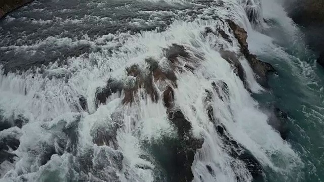 鸟瞰悬崖上汹涌的水流。一架直升机飞过冰岛的大瀑布