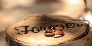 结婚戒指躺在树桩木制的乡村风格与碑文'永远'的仪式上的新郎和新娘