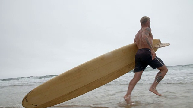 一个50岁以上的冲浪者拖着他的长板进入海浪。