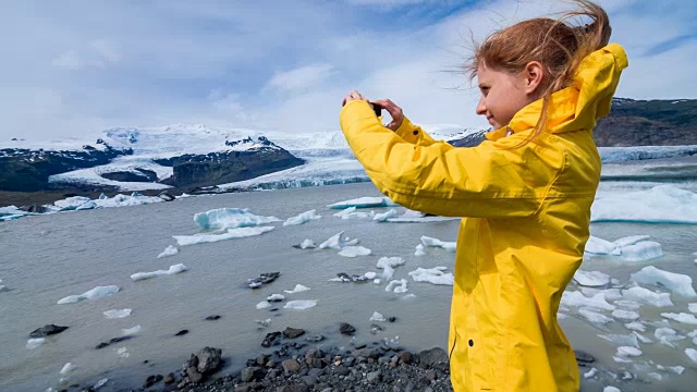在一个刮风的日子里，一名妇女在冰川泻湖上拍摄漂浮的冰山