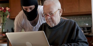 一名黑客在电脑上查看一位毫无戒心的老人的私人信息