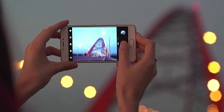 一名女子在日落时分用智能手机拍摄城市照片