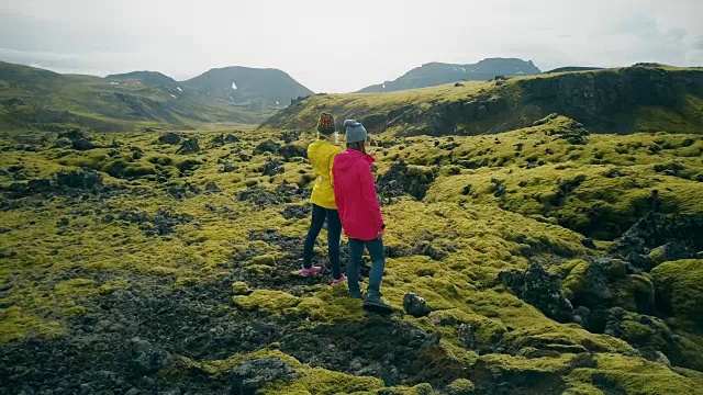 两名妇女在冰岛熔岩上行走的鸟瞰图。游客欣赏风景，探索领土