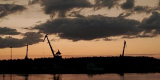 初夏的伏尔加河上，港口起重机在日出天空下的剪影