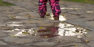 漂亮的小女孩穿着温暖的粉色工装裤跑过水坑。