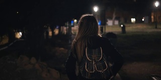 年轻时尚的女人走在深夜穿过黑暗的公园的背影。晚上一个人去