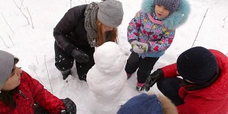 一家人带着孩子在公园里堆雪人。