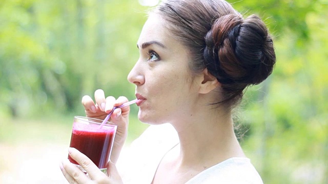 蔬菜排毒净化奶昔-女人通过吸管饮用。女孩喝红果汁。在户外。饮食和健康生活方式的概念