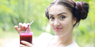 蔬菜排毒净化奶昔-女人通过吸管饮用。女孩喝红果汁。在户外。饮食和健康生活方式的概念