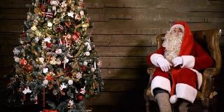 圣诞老人坐在圣诞树旁，拿着一个装满礼物的袋子