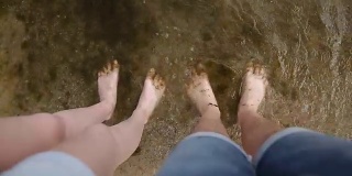 一对年轻夫妇的双腿一起站在海滩脏水里的沙子上。人们光着脚站在沾满海藻的肮脏海水里。环境污染的概念。