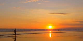 慢镜头:日落时分，一个不知名的跑步者在海边的沙滩上慢跑
