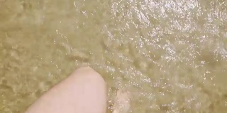 白种人的双腿在海边的金色沙滩上，高高地观看。光脚踩在海马上的人，脚被水覆盖着。夏天和放松的概念。阳光照在水面上。