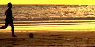 日落时分，十几岁的孩子们在海边的沙滩上踢足球