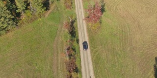 空中的黑色SUV汽车驶过彩色的树木和草地在阳光明媚的秋天