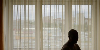 窗户前，一名男子在家打太极的剪影。早上亚洲实践。锁在家里。