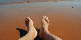 男人的腿躺在沙滩上