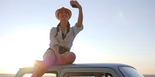 女孩对着海边的老爷车车顶自拍，女人对着老机器用手机拍照