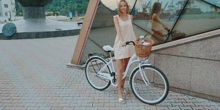 户外时尚肖像优雅的金发女士站在她的时髦复古自行车在时尚的衣服。享受夏日，在港口摆好姿势。女孩微笑。慢动作