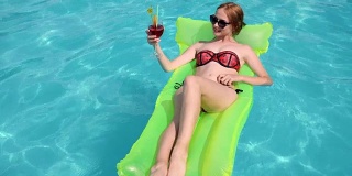 水派对，女孩在比基尼躺在充气海滩床垫到泳池边，女性在游泳衣与五颜六色的鸡尾酒在手里