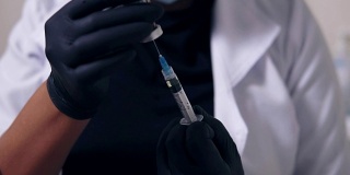 近距离观看一个不认识的专业医生在黑色手套和口罩与医疗注射器在手中，准备注射