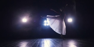 一个穿着飘逸长裙的单身芭蕾舞女演员在黑暗中表演。4 k。