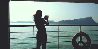 年轻的黑发女子站在游轮救生圈的甲板上，用智能手机用慢动作拍照。1920 x1080,高清