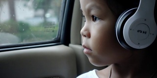 亚洲漂亮的女孩听音乐耳机移动在汽车和看在雨天